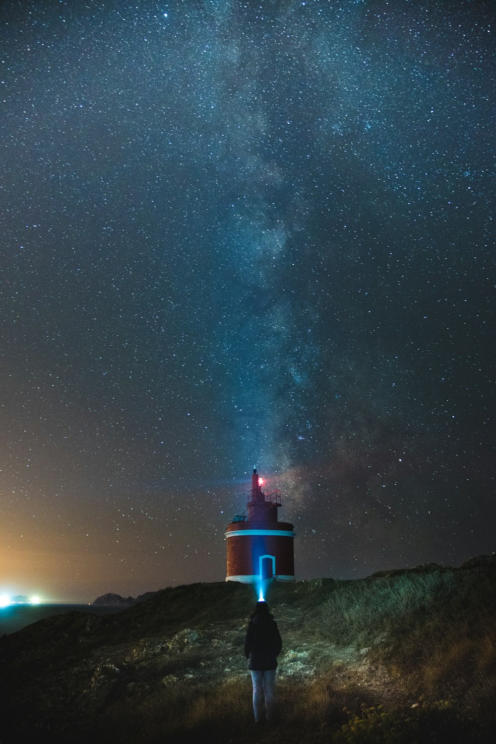 person walking towards red and white lighthouse under starry sky