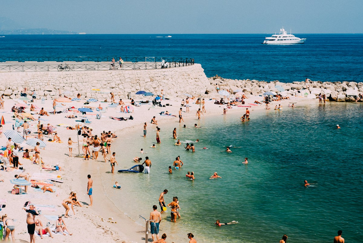 A crowded Mediterranean beach with a yacht anchored offshore