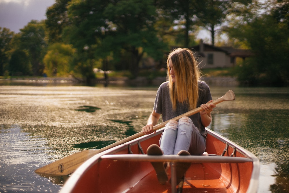 woman riding on canoe on body of water near tall trees at daytime