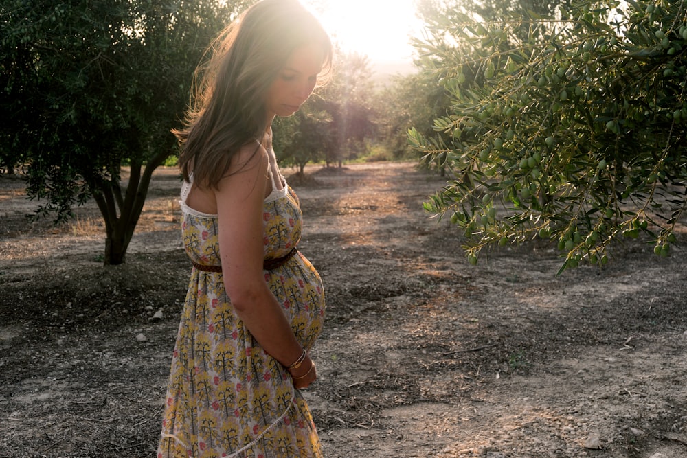 pregnant woman wearing beige and red floral sleeveless dress standing near plant