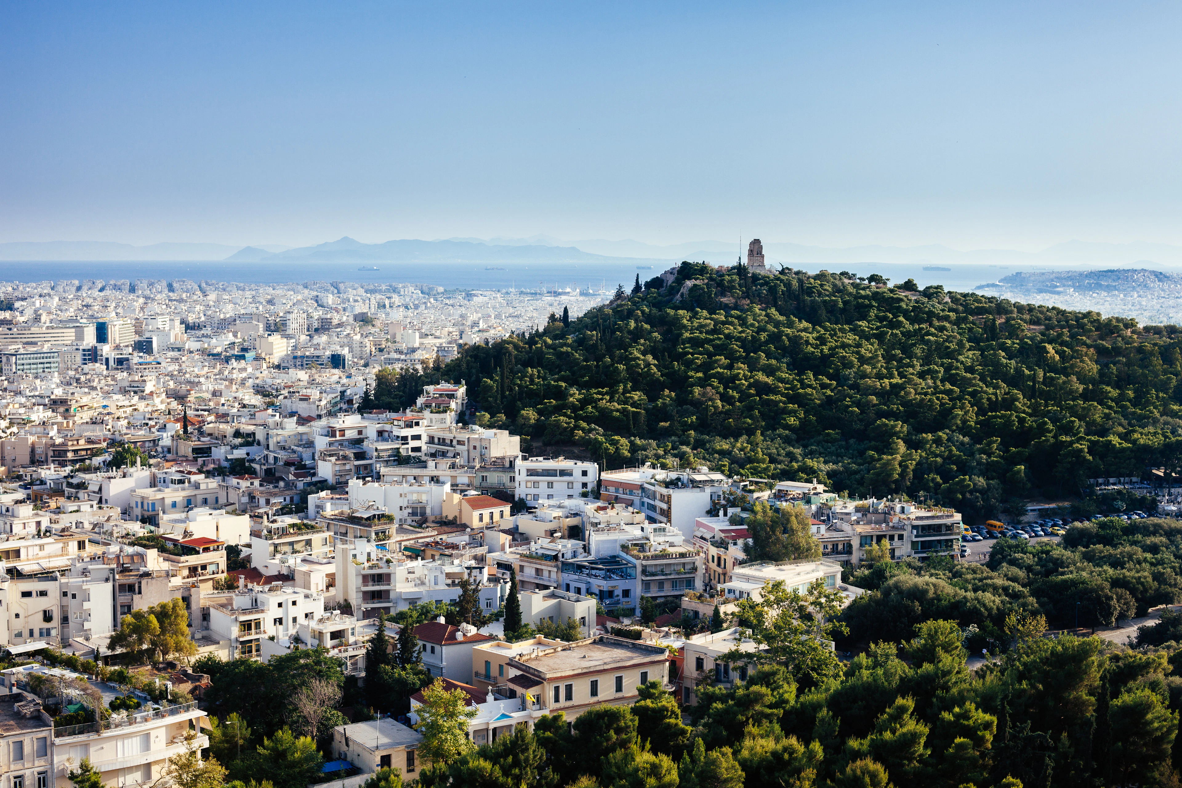 Lycabettus Hill rising green out of the white sprawl of Athens, mountains along the horizon