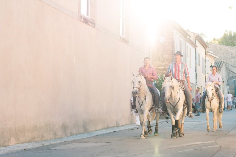 three men riding horses near white concrete building during daytime