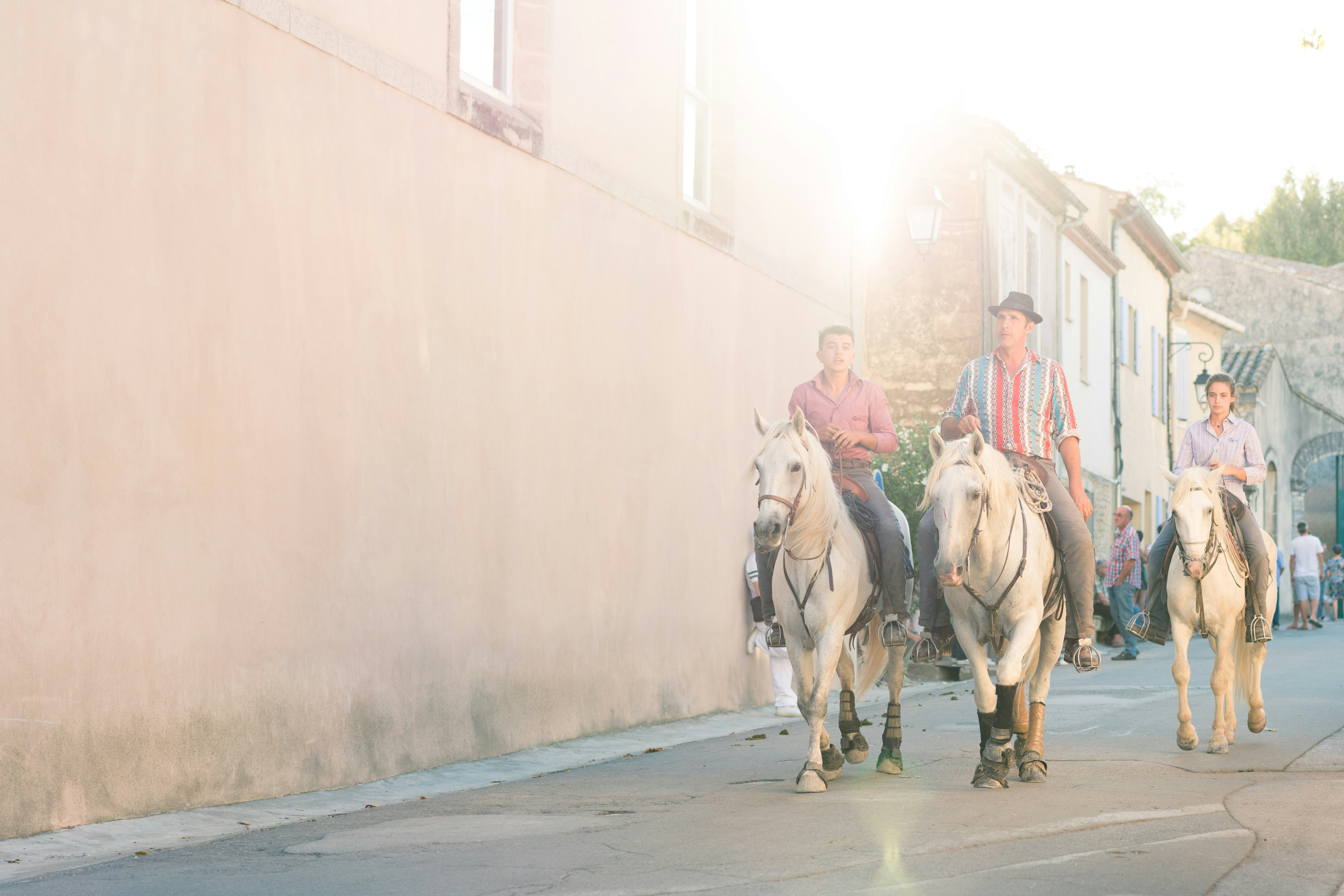 three men riding horses near white concrete building during daytime