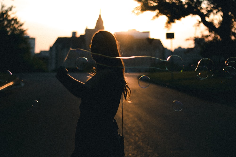 silhouette photo of woman holding bubbles near building during golden hour