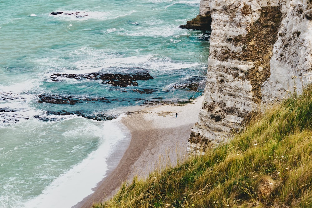 beige rugged cliff beside body of water at daytime