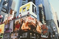 Billboards and advertisements dominate the urban landscape, showcasing products, brands, and entertainers. The scene is bustling with bright signage against the backdrop of towering skyscrapers and city structures.