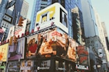 Billboards and advertisements dominate the urban landscape, showcasing products, brands, and entertainers. The scene is bustling with bright signage against the backdrop of towering skyscrapers and city structures.