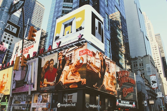Billboards and advertisements dominate the urban landscape, showcasing products, brands, and entertainers. The scene is bustling with bright signage against the backdrop of towering skyscrapers and city structures.