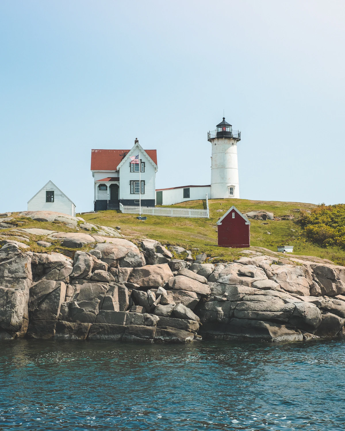 A New England lighthouse on a rocky coastline at dusk
