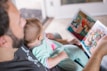 An adult is reading a colorful picture book to a baby who is sitting on their lap. The baby is dressed in pajamas with a cute design. The setting appears to be indoors with soft, natural light illuminating the scene.