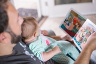 person carrying baby while reading book