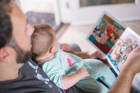 man carrying baby and reading children's book