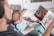 An adult is reading a colorful picture book to a baby who is sitting on their lap. The baby is dressed in pajamas with a cute design. The setting appears to be indoors with soft, natural light illuminating the scene.