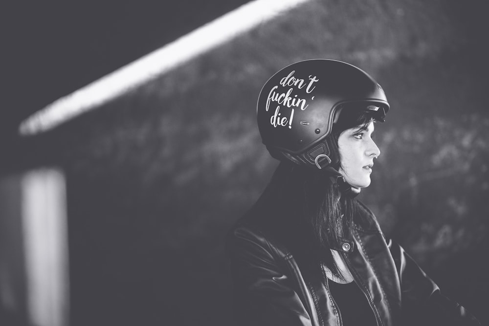 革のジャケットと半顔のオートバイのヘルメットをかぶった女性のグレースケール写真