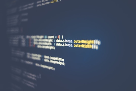 A close-up view of a computer screen displaying lines of code. The code features syntax elements like variables, functions, and brackets, highlighted in different colors against a dark background. The text is slightly out of focus along the edges, with a more focused section in the middle.