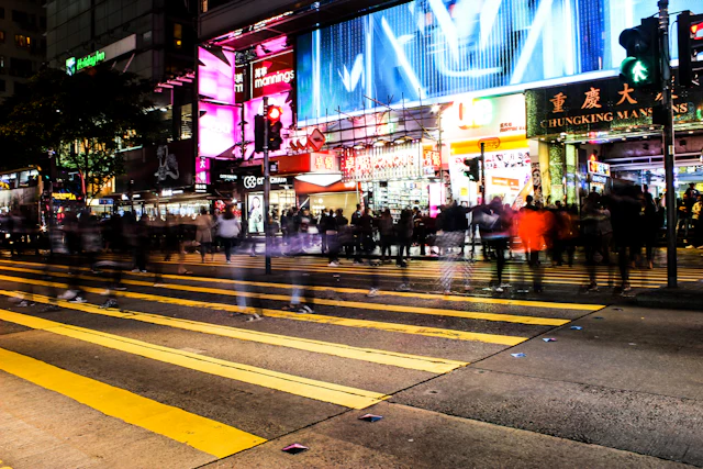 Night street scene in Tsim Sha Tsui with neon signage including the Chungking Mansions sign over a busy crosswalk.