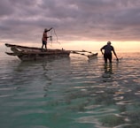 Two fishermen laughing together on a small boat at sunrise.