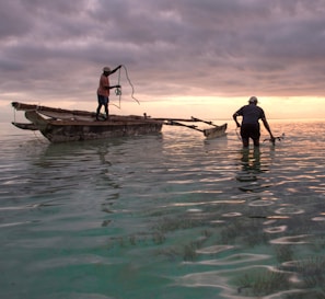 Two fishermen laughing together on a small boat at sunrise.