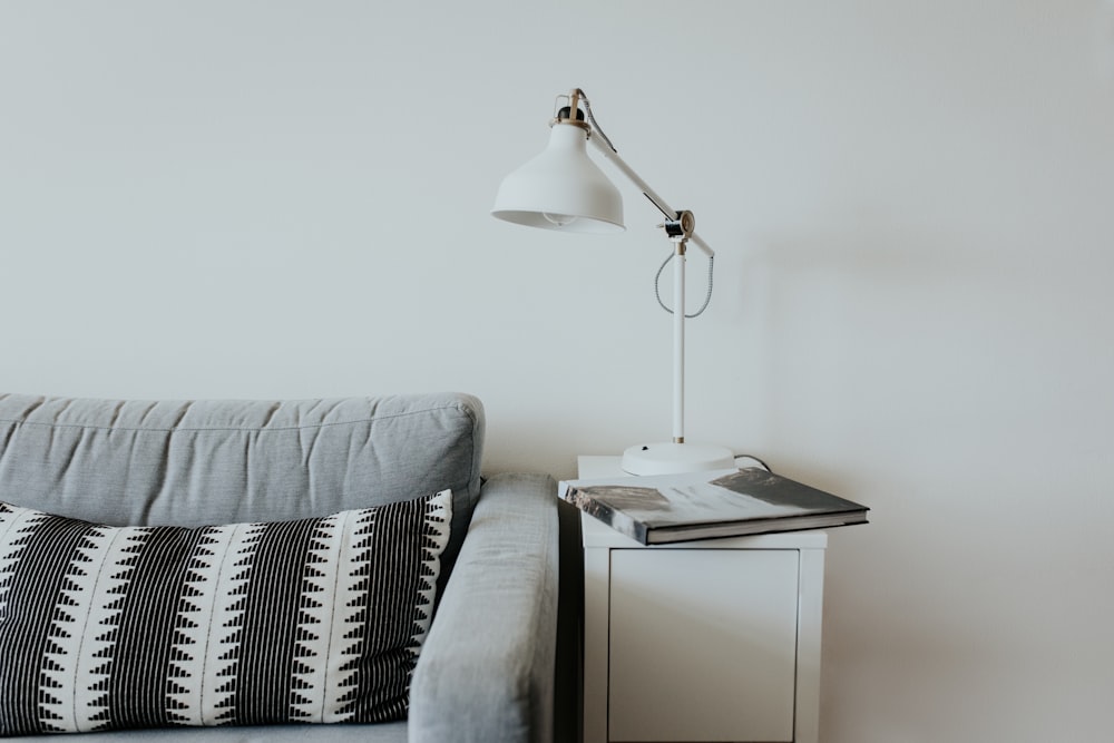 lampe de bureau blanche près du canapé en tissu gris