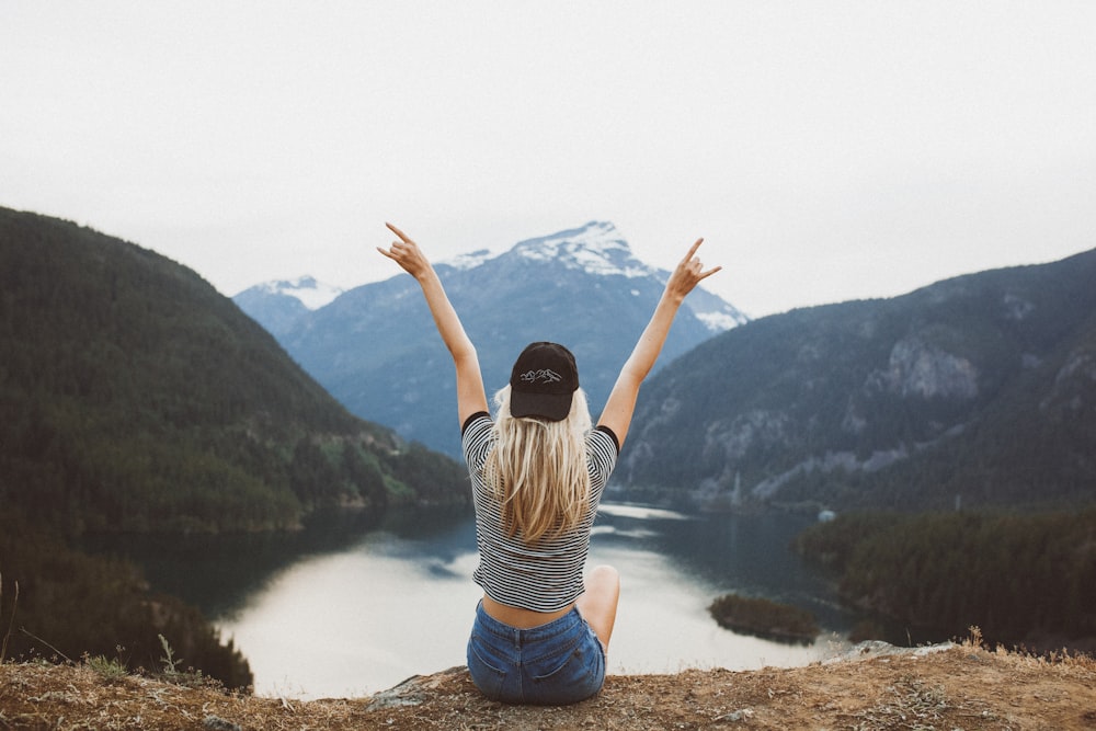 woman sitting on cliff raising both hands