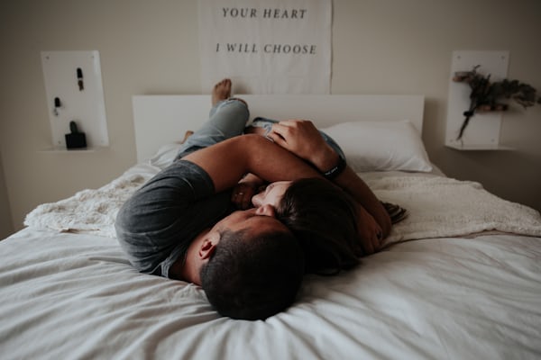 One man and woman lean close on the bed