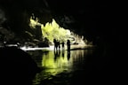 A group of tourists exploring a cave surrounded by tropical vegetation.