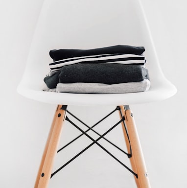 pile of black, white, and gray textiles on white padded chair with brown frame