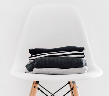 pile of black, white, and gray textiles on white padded chair with brown frame