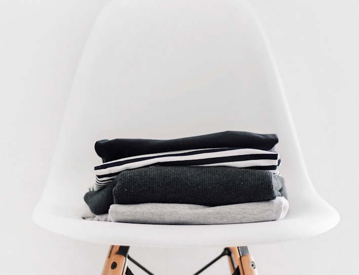 pile of black, white, and gray textiles on white padded chair with brown frame