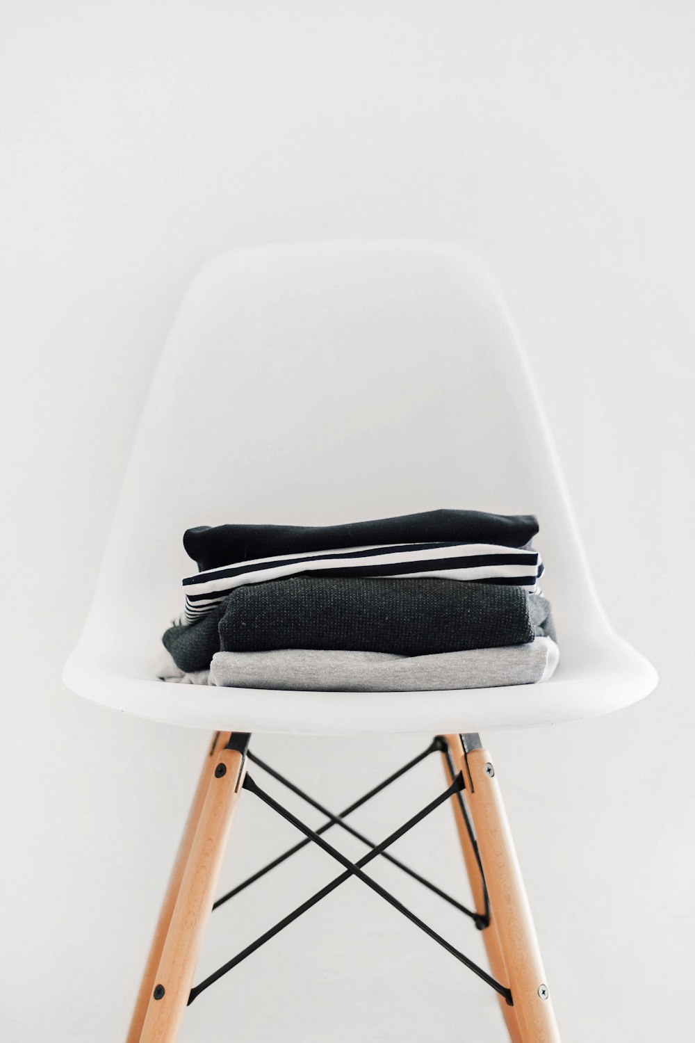 pile of black, white, and gray textiles on white padded chair with brown frame