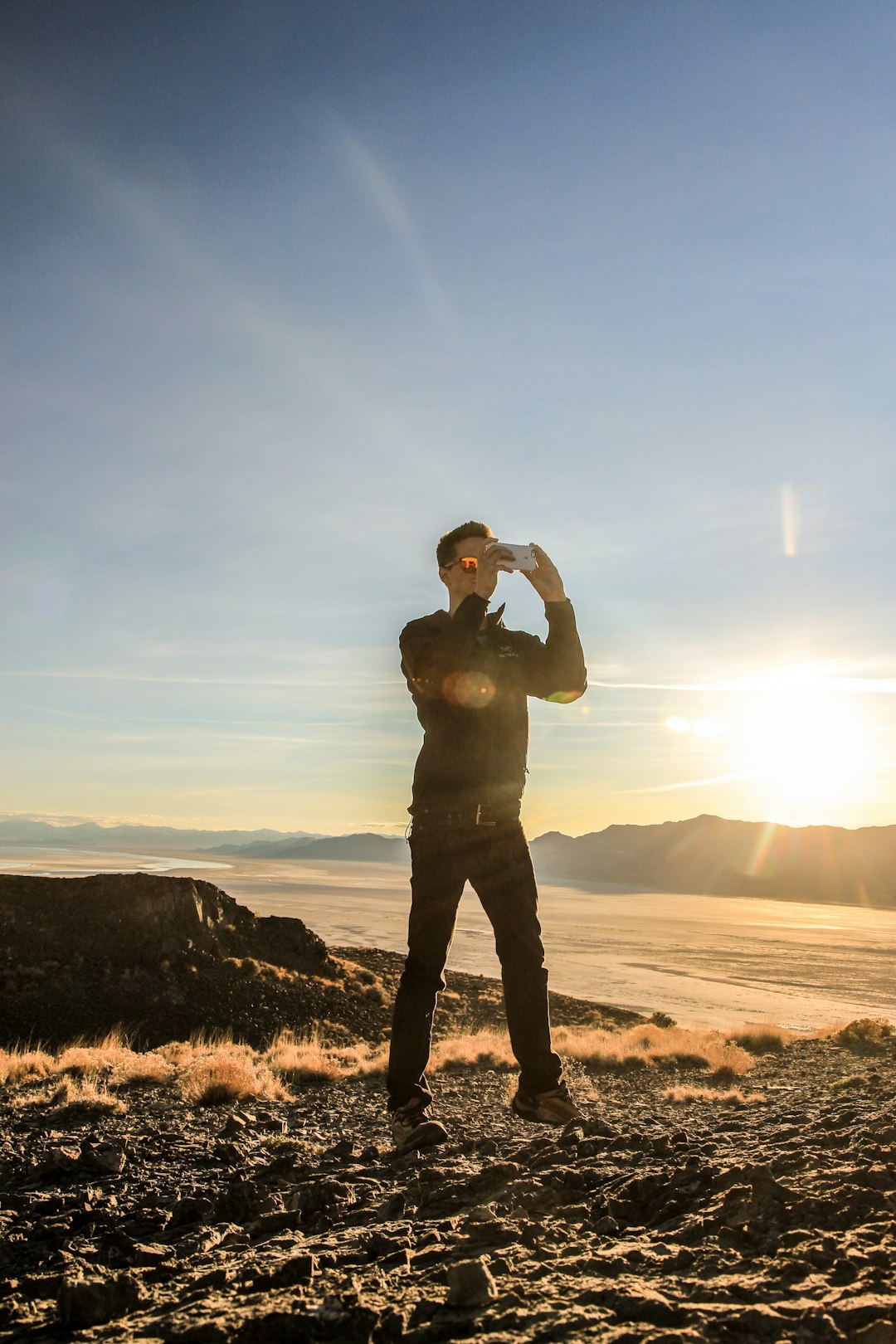 man in black jacket standing on brown sand during sunset