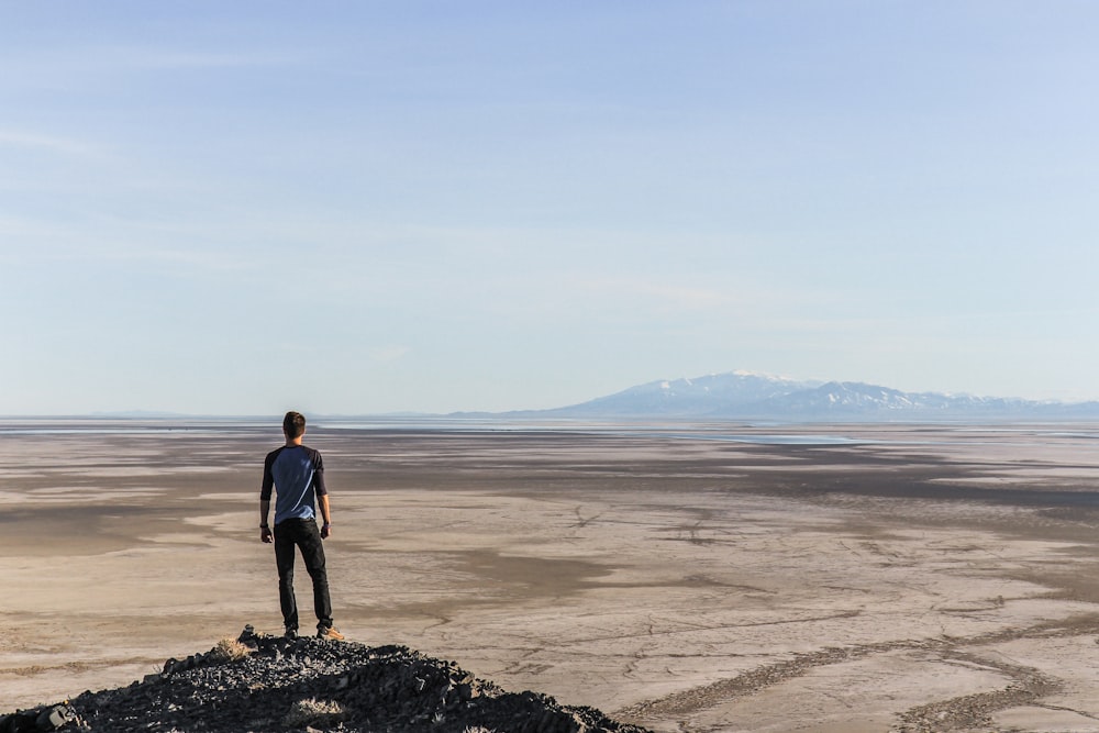 man standing on top of mountain overlooking desert during daytime