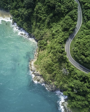 A winding coastal road with turquoise waters on one side and volcanic cliffs on the other in Réunion.
