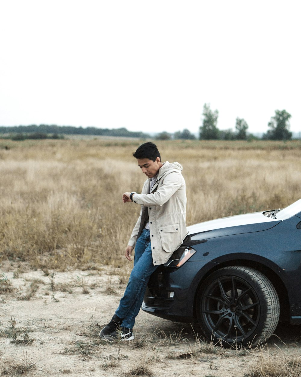 man sitting on car while looking at watch