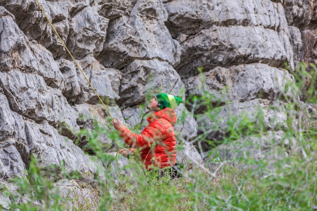 man in red jacket climbing on rocky mountain during daytime