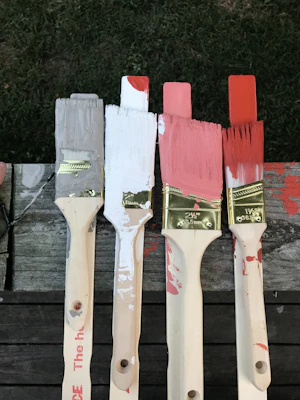 A close-up of paint brushes and rollers with red, white, and blue paint on a clean drop cloth.