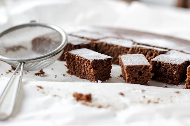 Close-up of a rustic chocolate zucchini cake with a dusting of powdered sugar on a wooden table.