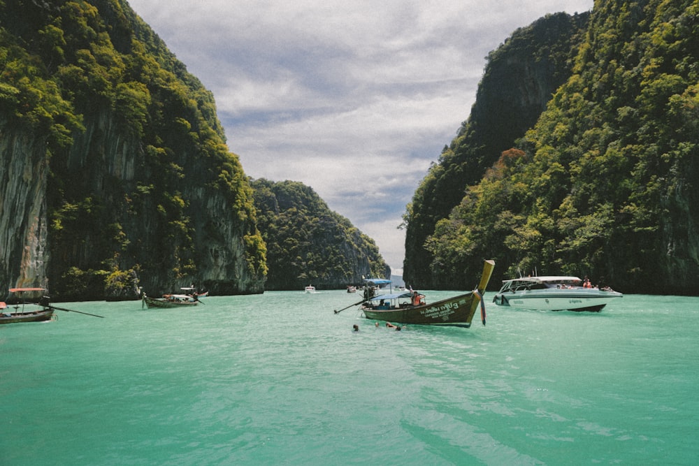 Canoes and motor powered boats driving in bluish green water under mountains.
