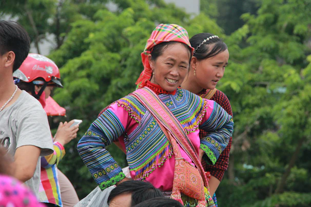 A joyful young woman wearing a colorful Pakistani dress, smiling on a university campus.