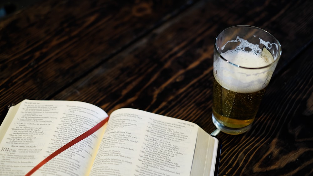 clear drinking glass filled with brown liquid near open book