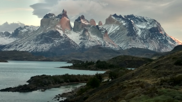A breathtaking view of Patagonia's snow-capped mountains reflected in a crystal-clear lake at sunset.