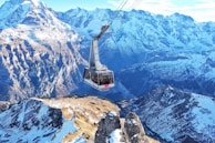 A cable car suspended over a breathtaking valley with rolling hills and distant peaks.