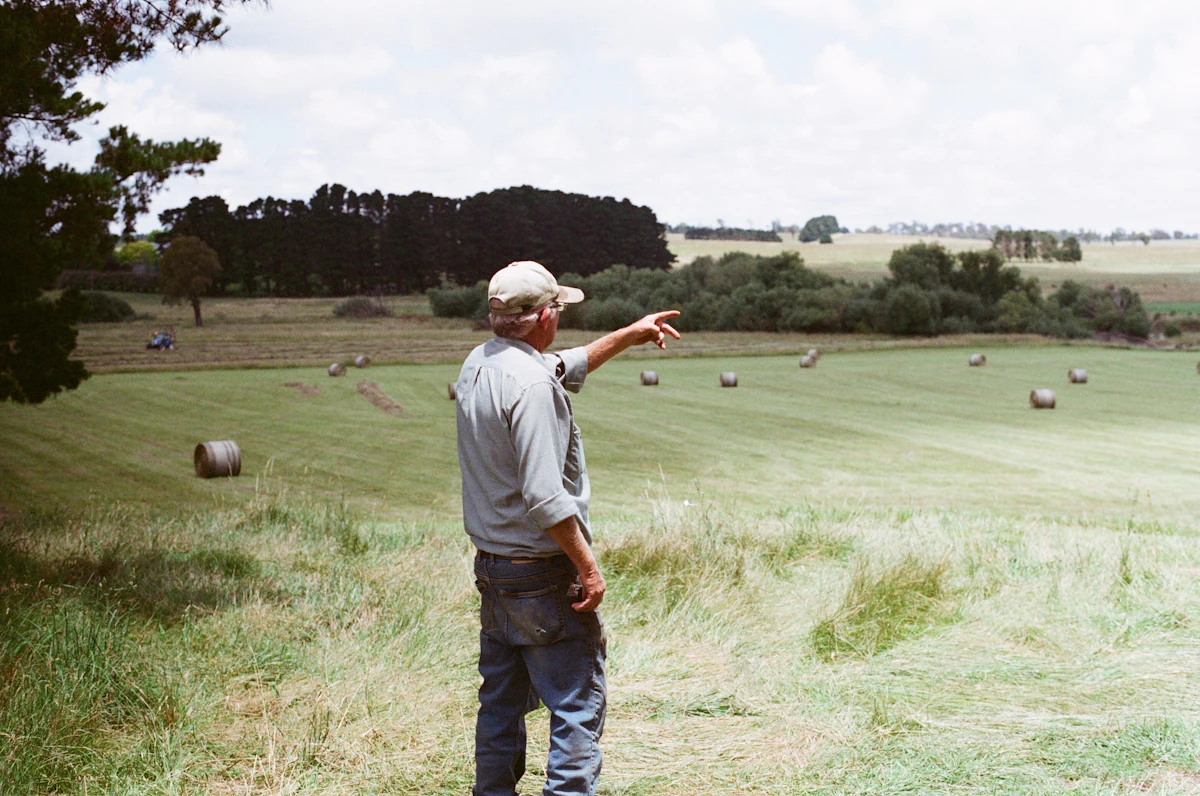 A farmer pointing across a paddock with hay bales