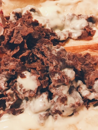 Thinly sliced, cooked meat topped with melted cheese, placed on a bread or flatbread base. The meal looks rich and savory with the cheese evenly distributed across the meat.