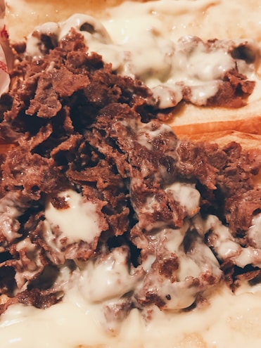 Thinly sliced, cooked meat topped with melted cheese, placed on a bread or flatbread base. The meal looks rich and savory with the cheese evenly distributed across the meat.