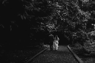 A cinematic candid of a couple walking hand in hand along a sandy path with charcoal shadows.