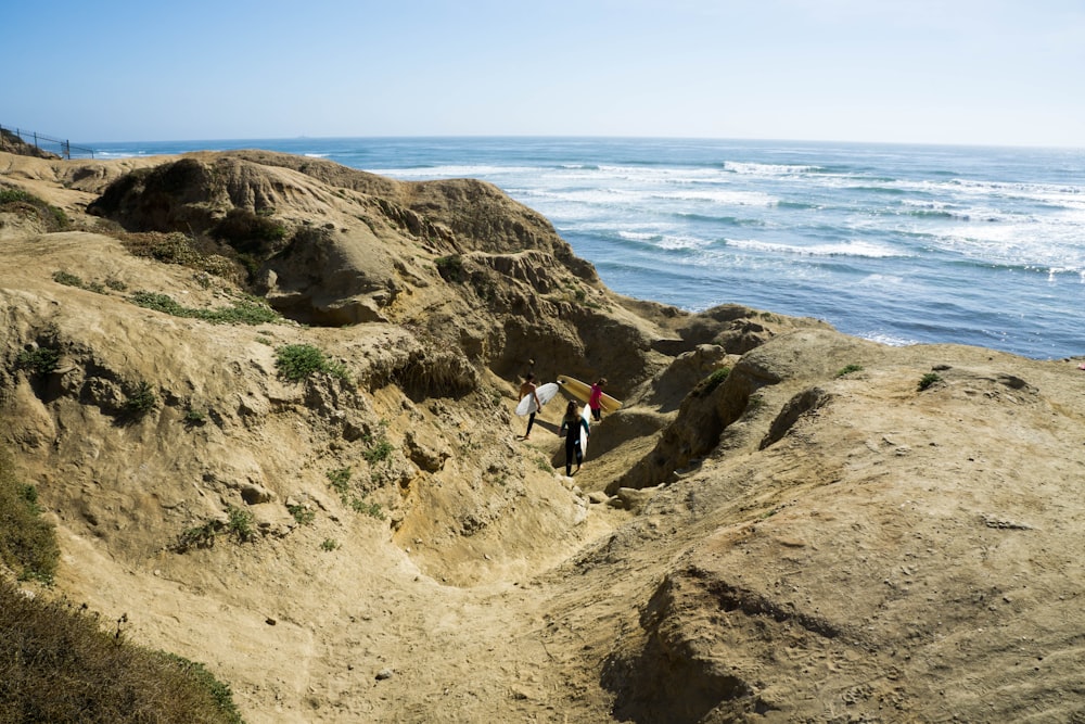 three persons carrying surfboards