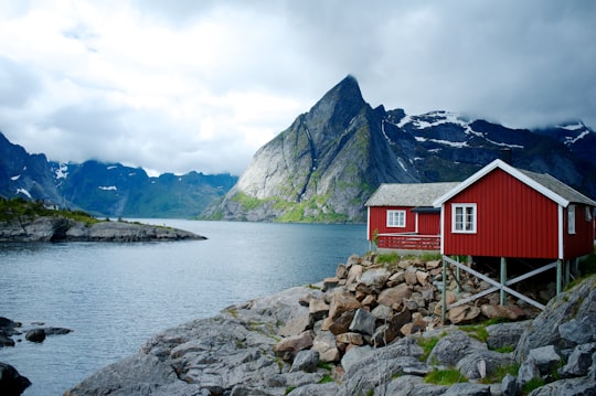 red and white wooden house in front of body of water in Hamnøy Norway