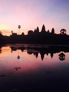A serene Balinese temple at sunset with vibrant orange skies reflecting on a tranquil pond.