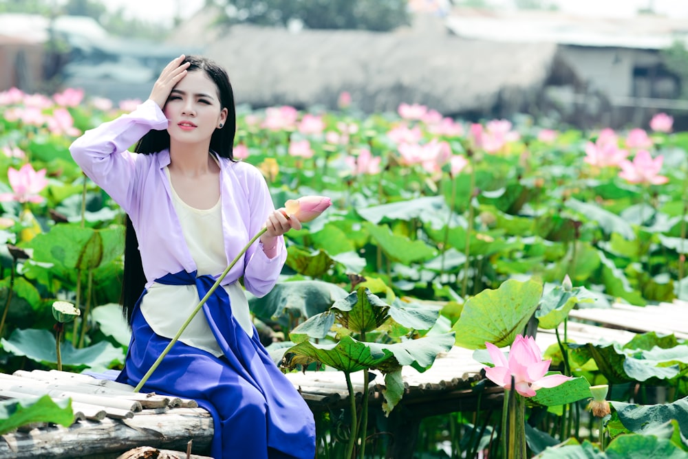 Photographie de décalage d’inclinaison de femme assise derrière des plantes à fleurs roses